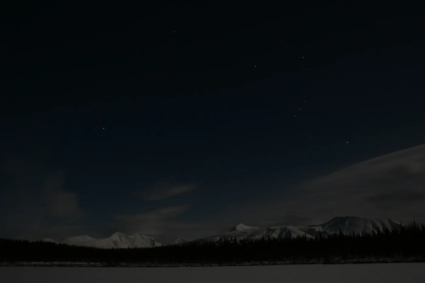 A clear, moonless Alaskan night — stars over snowy mountains and a frozen lake