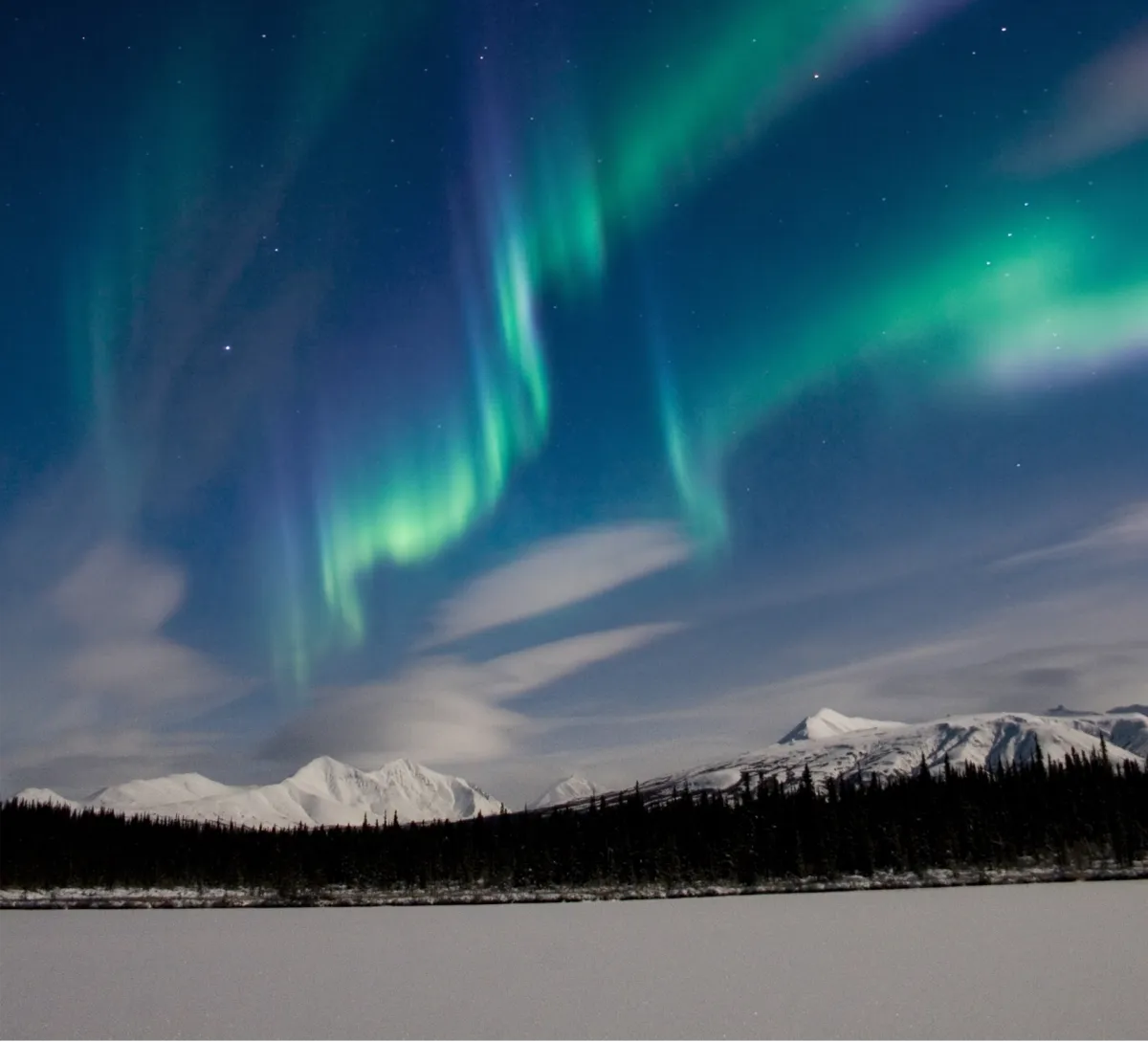 Green and violet aurora over snow-covered mountains and a frozen lake